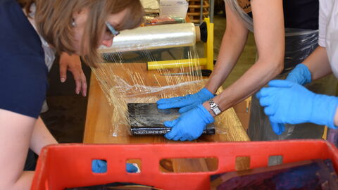 Drei Personen wickeln bei einem Notfallworkshop durchnässte Bücher in Stretchfolie ein.